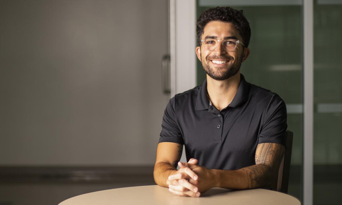 Image of a male student sitting at a table smiling at the camera