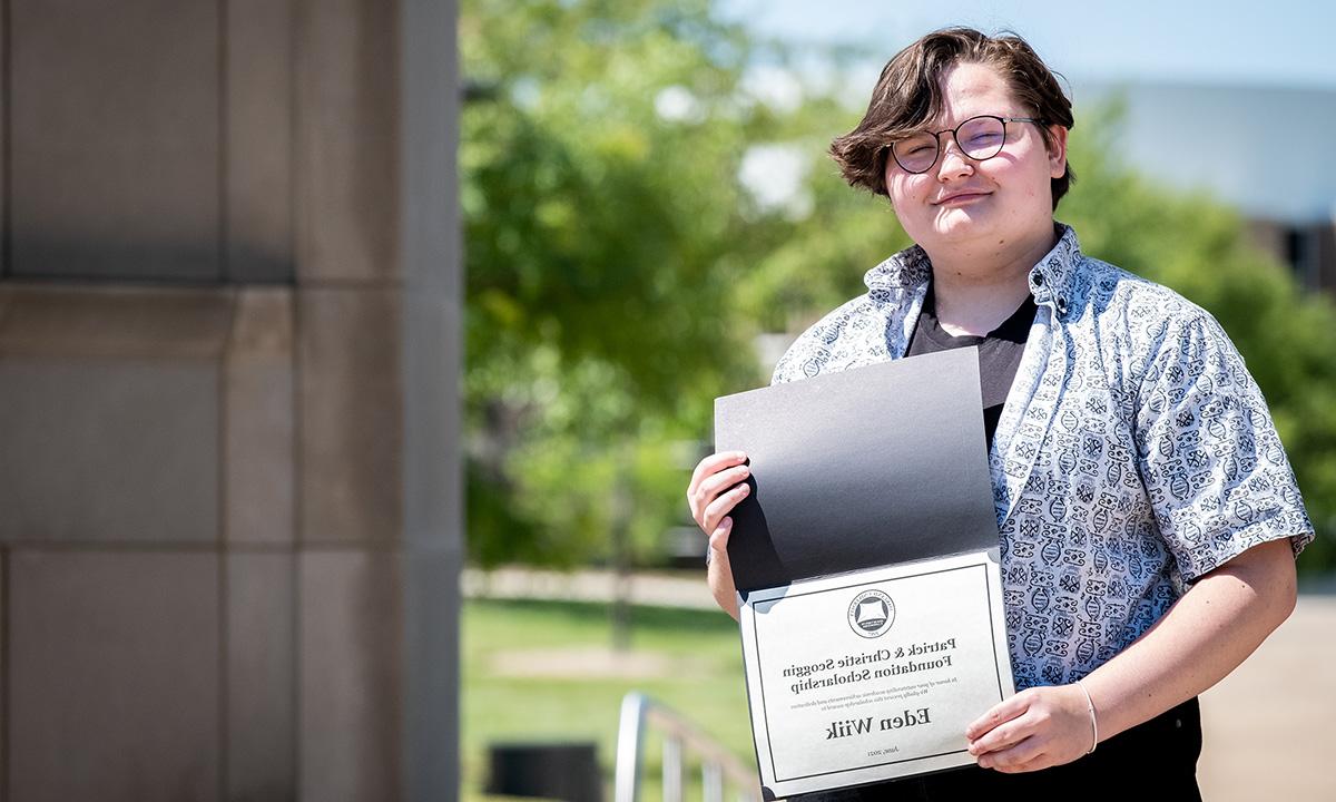 A woman holding a scholarship outside.